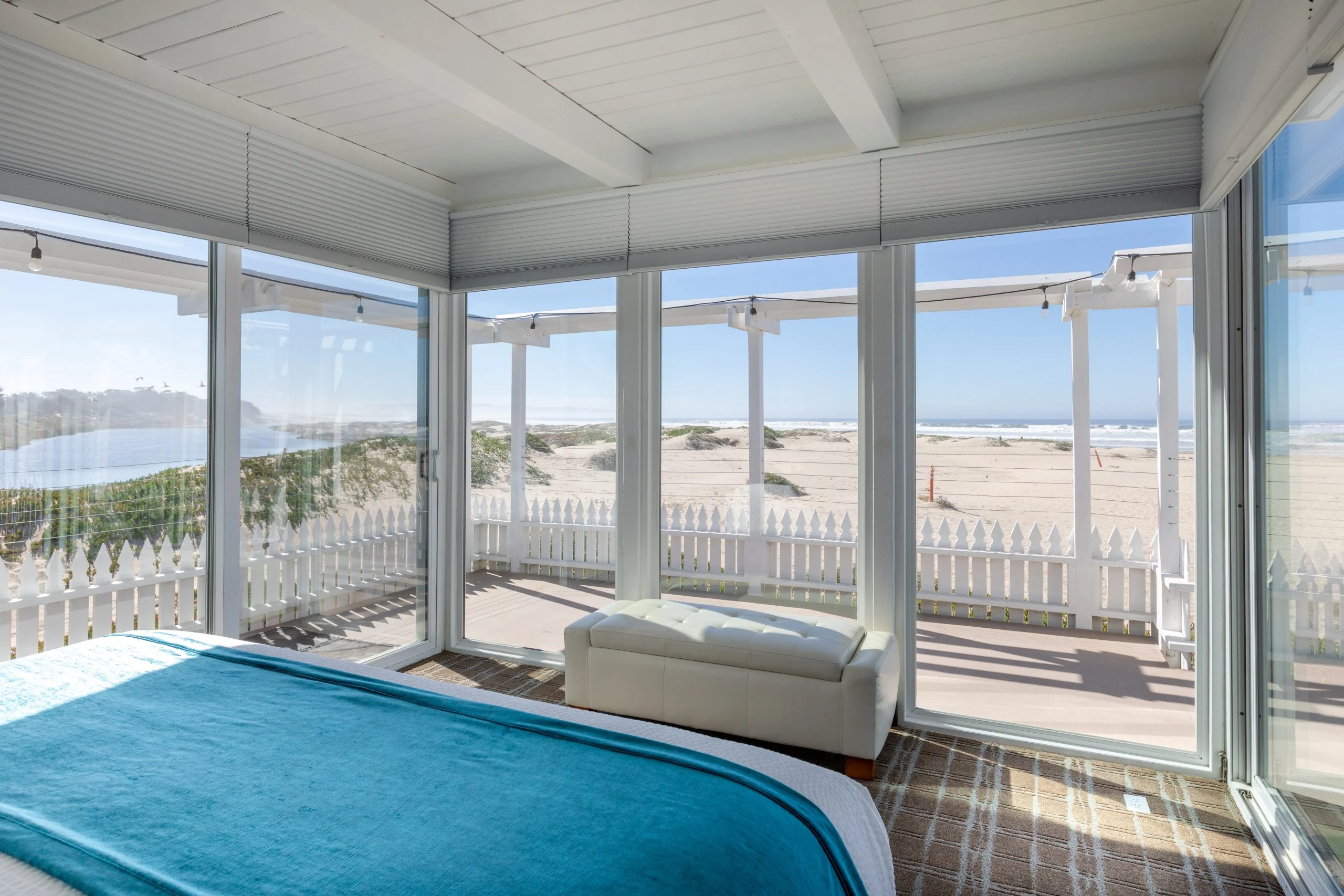 A beachfront hotel room with a large bed and expansive windows showing the ocean view.