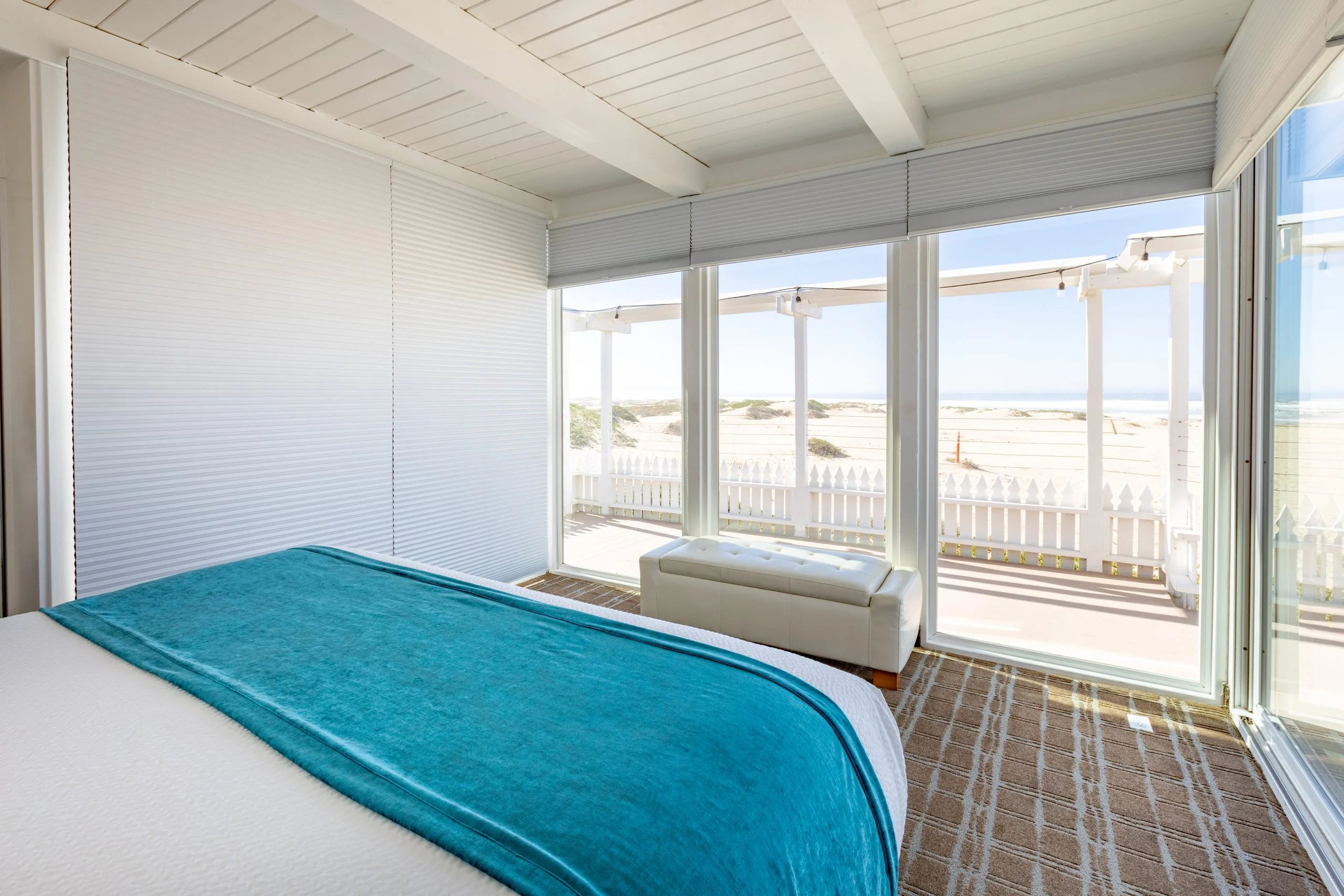 A beach-themed room with a bed, chaise lounge, and sliding doors leading to a beach view.